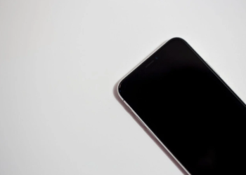Close-up of a dark smartphone corner with screen off, lying on a white surface