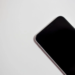 Close-up of a dark smartphone corner with screen off, lying on a white surface