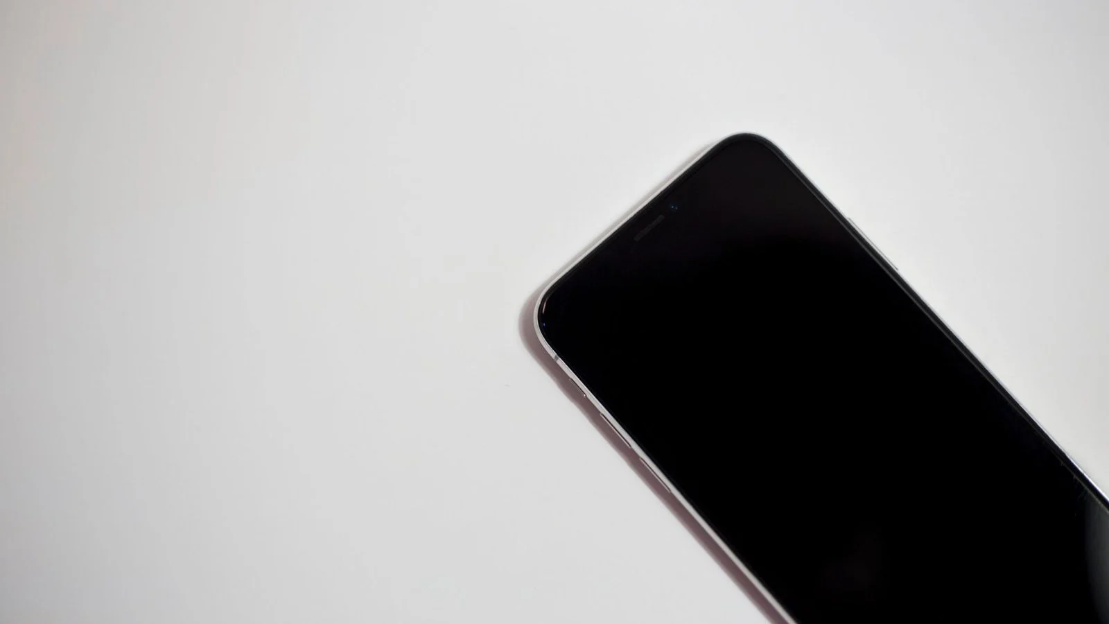 Close-up of a dark smartphone corner with screen off, lying on a white surface