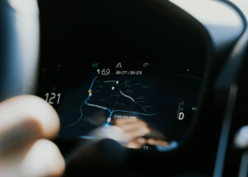 Blurred hand near a car instrument cluster showing a navigation map with a blue route line