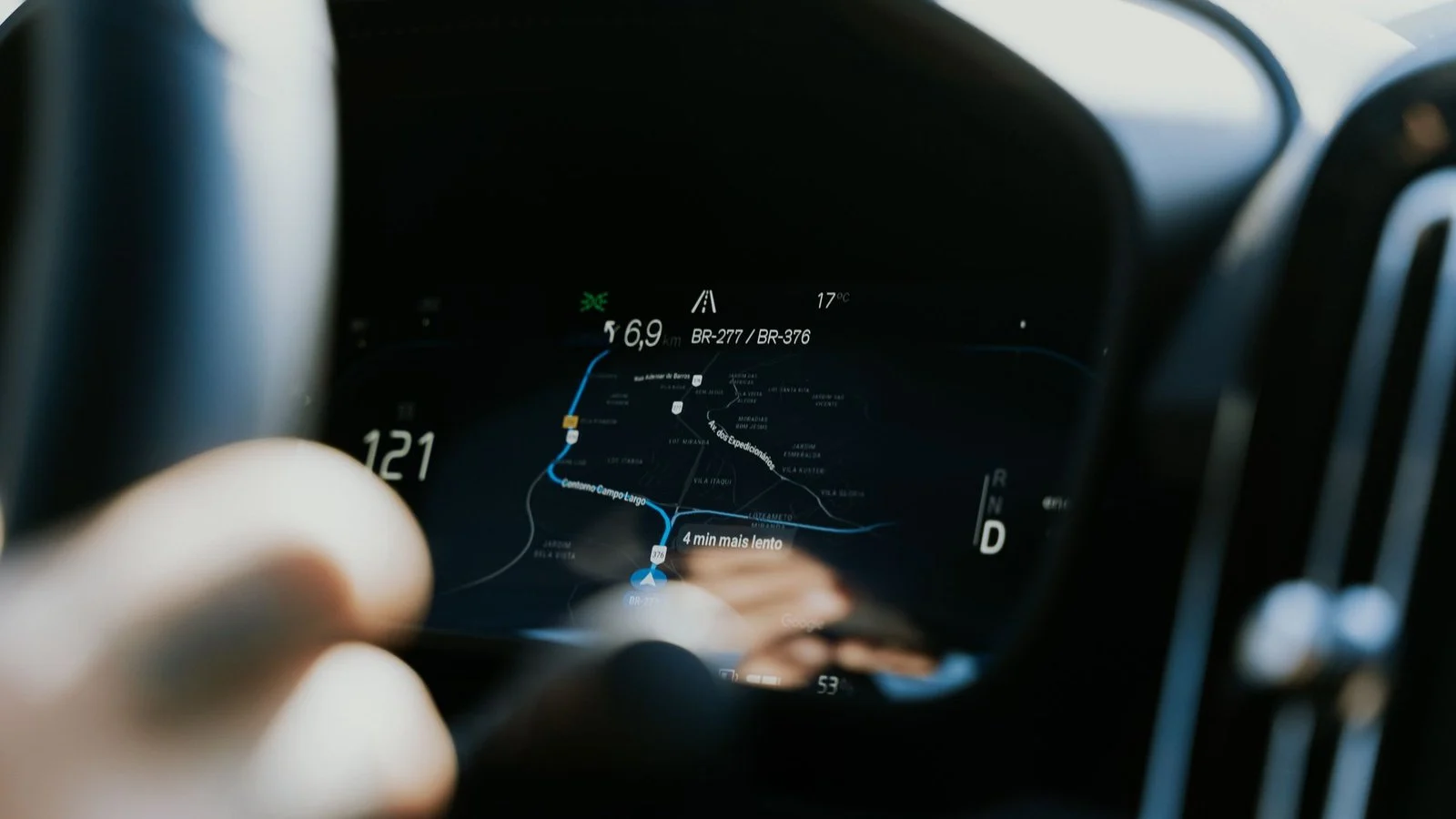 Blurred hand near a car instrument cluster showing a navigation map with a blue route line