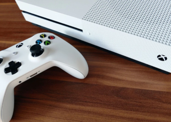 White Xbox One S console and matching white wireless controller on a wooden desk