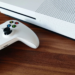White Xbox One S console and matching white wireless controller on a wooden desk