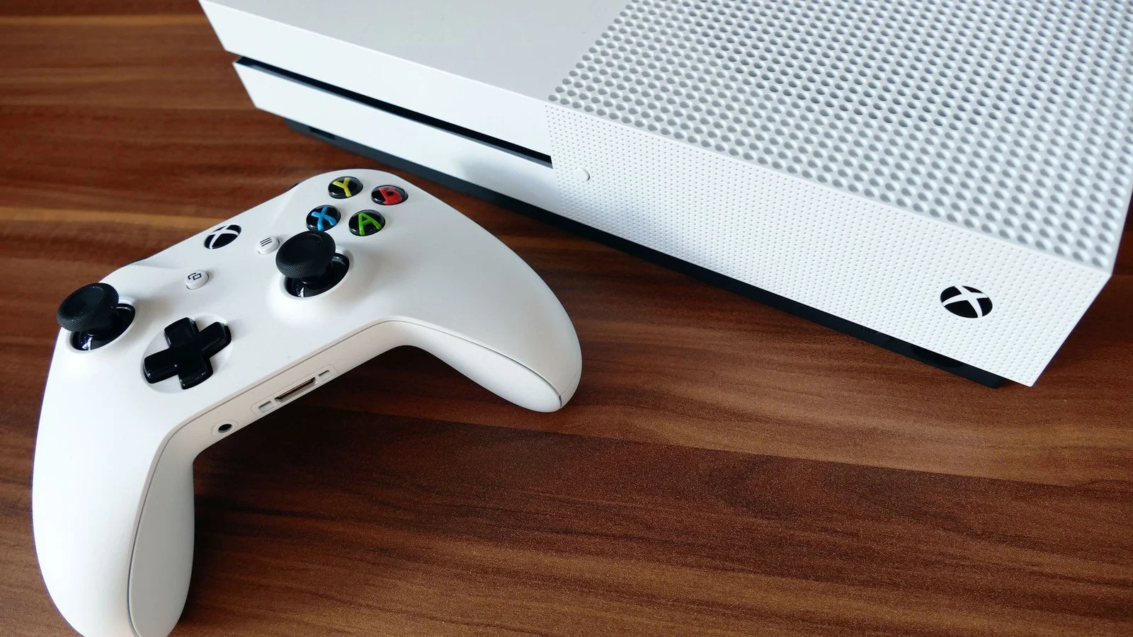 White Xbox One S console and matching white wireless controller on a wooden desk