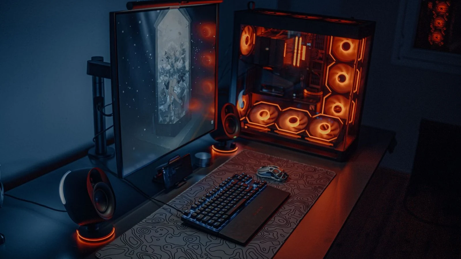 Gaming PC tower with orange RGB fans next to a monitor and mechanical keyboard on a desk