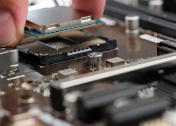 A hand lowers a silver processor chip into an empty socket on a motherboard