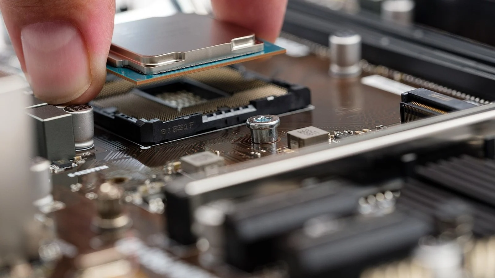 A hand lowers a silver processor chip into an empty socket on a motherboard
