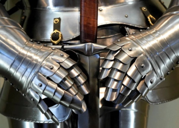 Close-up of steel plate armor gauntlets gripping a sword hilt against the chest