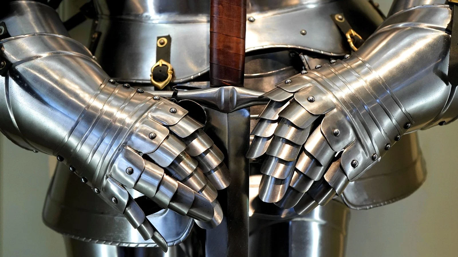 Close-up of steel plate armor gauntlets gripping a sword hilt against the chest