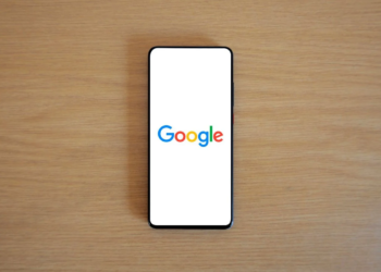 Black-bezeled smartphone lying flat on wood desk, screen showing the Google logo