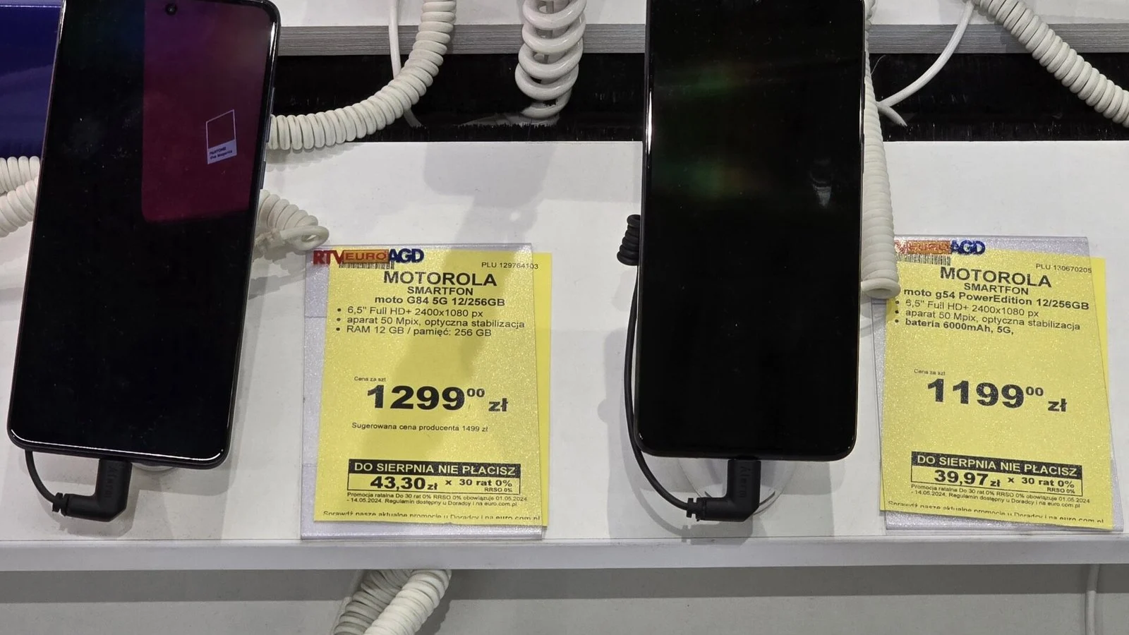 Two Motorola smartphones on security cables at a store display next to yellow Polish price tags