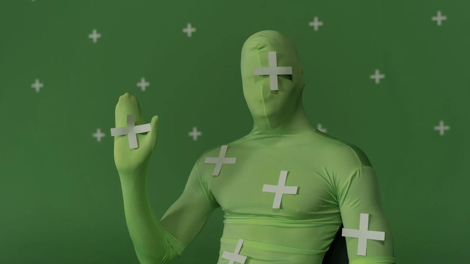Person in green motion-capture suit with white tracking markers against a green screen backdrop