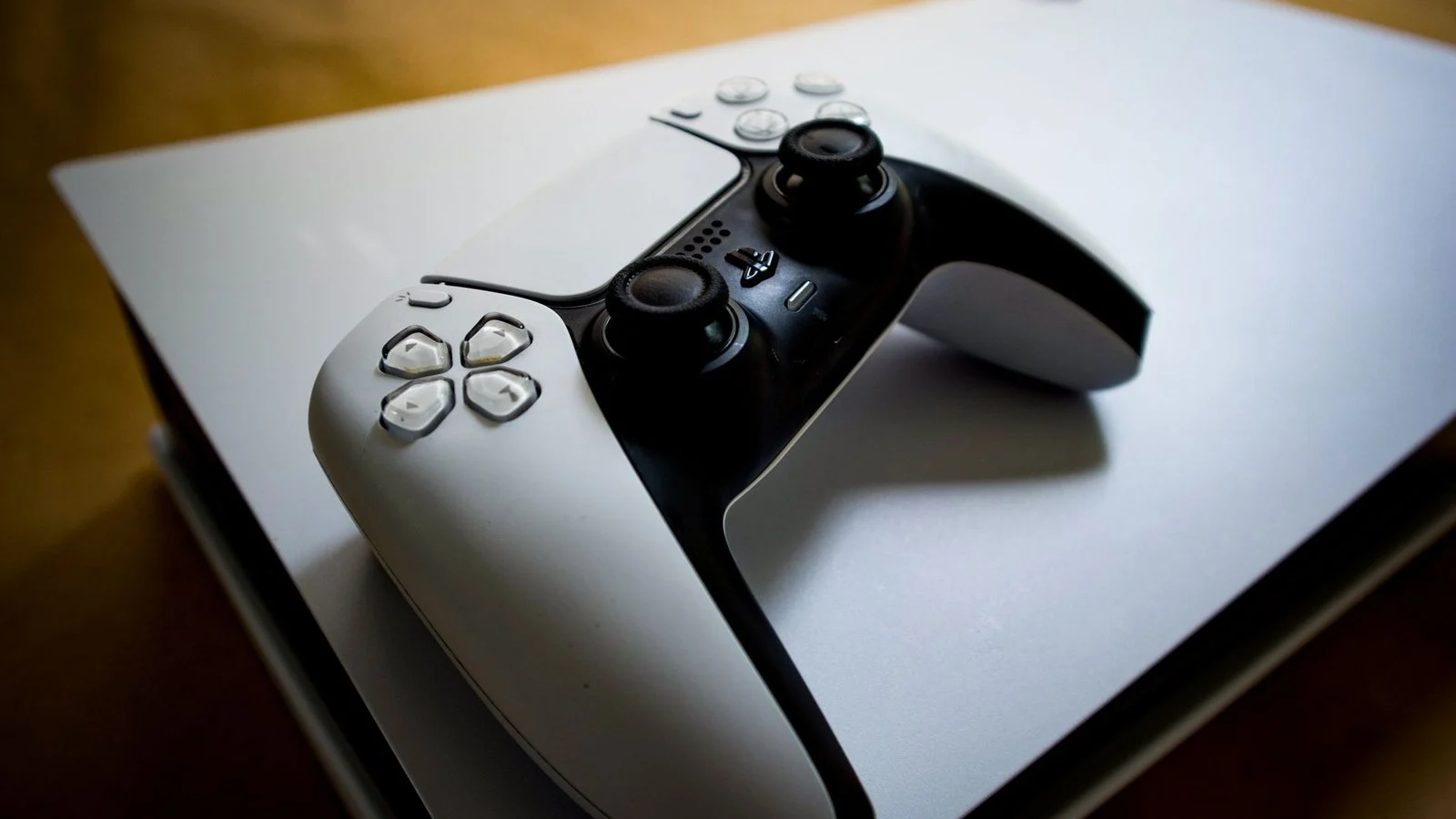 A white DualSense controller resting on top of a white PlayStation 5 console