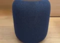 A dark blue mesh-covered cylindrical smart speaker on a wooden surface