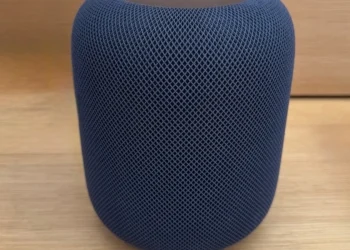 A dark blue mesh-covered cylindrical smart speaker on a wooden surface