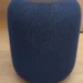 A dark blue mesh-covered cylindrical smart speaker on a wooden surface