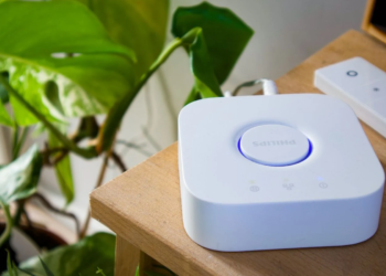 White square Philips Hue smart home bridge with glowing blue ring beside a remote on a table