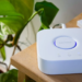 White square Philips Hue smart home bridge with glowing blue ring beside a remote on a table