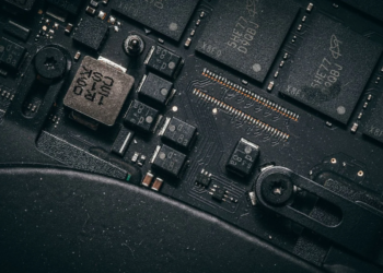 Close-up of a dusty laptop circuit board with black memory chips and screws