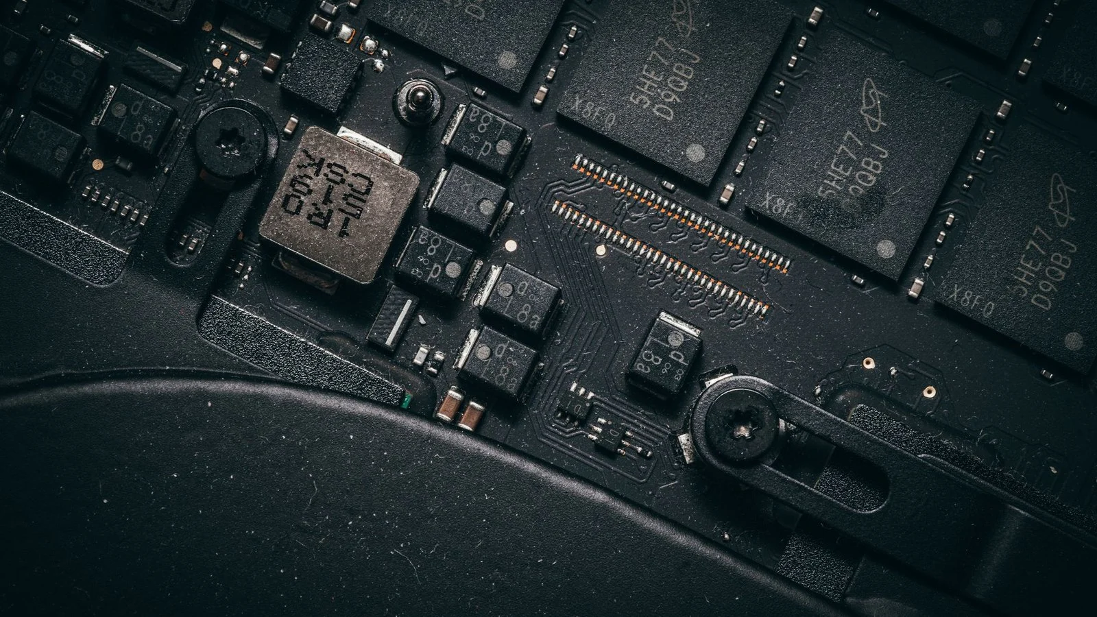Close-up of a dusty laptop circuit board with black memory chips and screws