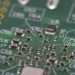Close-up of a green circuit board with surface-mount components and labeled capacitor pads