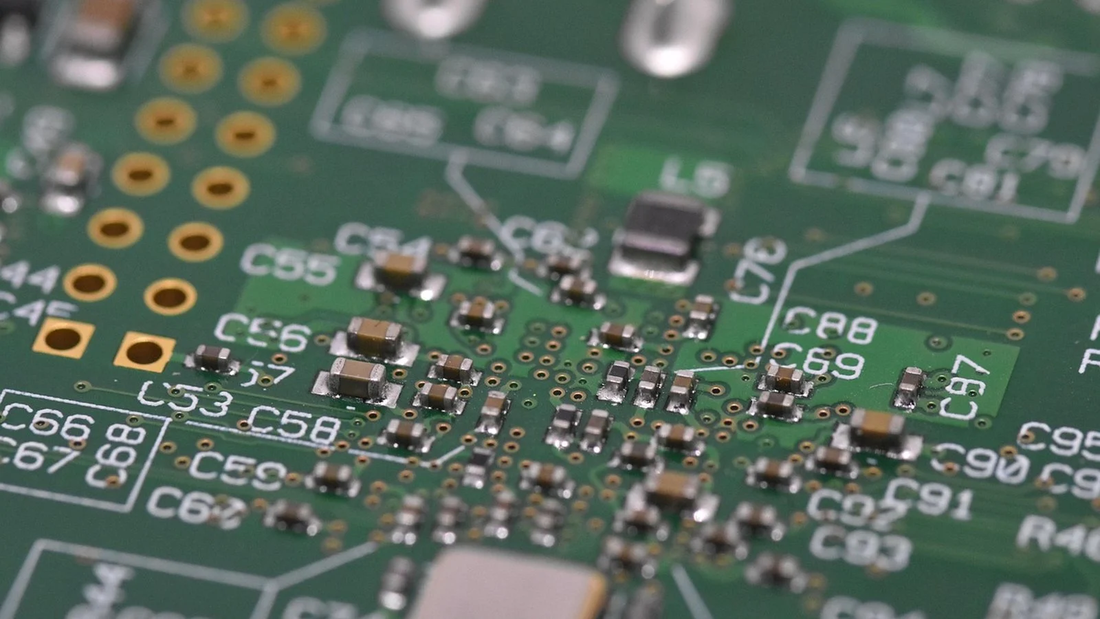 Close-up of a green circuit board with surface-mount components and labeled capacitor pads