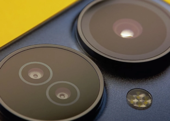 Macro shot of a dark smartphone's circular rear camera lenses and flash on a yellow background