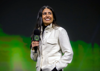 Woman in white jacket holding an Xbox-branded microphone on stage in front of green lighting