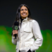 Woman in white jacket holding an Xbox-branded microphone on stage in front of green lighting
