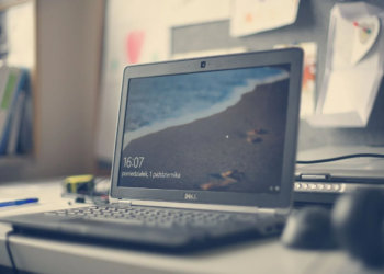 A black Dell laptop open on a white desk in an office, its lid logo visible and a Windows lock screen on the display
