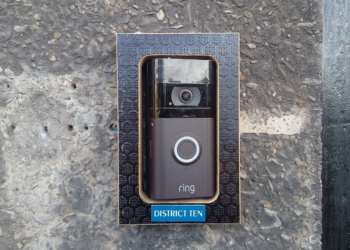 A Ring video doorbell with camera and glowing blue button mounted on a stone wall