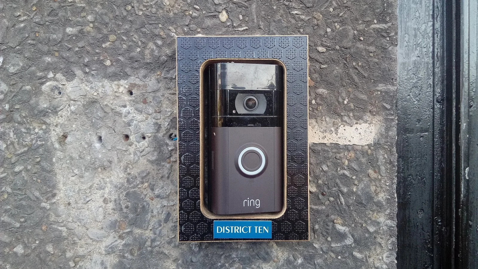 A Ring video doorbell with camera and glowing blue button mounted on a stone wall