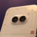 Close-up of a white smartphone's transparent back panel with visible screws and a pill-shaped dual-camera module