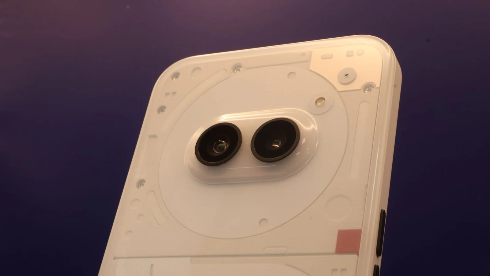 Close-up of a white smartphone's transparent back panel with visible screws and a pill-shaped dual-camera module