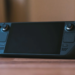 A black handheld gaming console with dual grips and joysticks resting on a wooden table, screen off