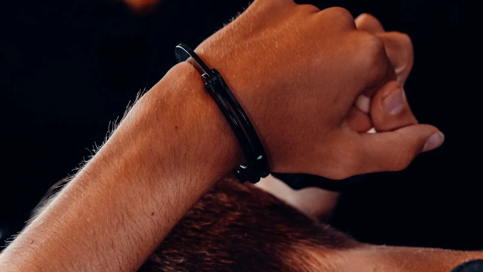 Close-up of a person's wrists bound behind their back in steel handcuffs