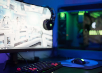 Gaming PC desk with curved monitor showing a game, headphones hooked on it, RGB tower and mouse