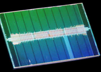 Macro photo of a rectangular silicon chip die with green and blue circuit block patterns