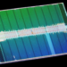 Macro photo of a rectangular silicon chip die with green and blue circuit block patterns