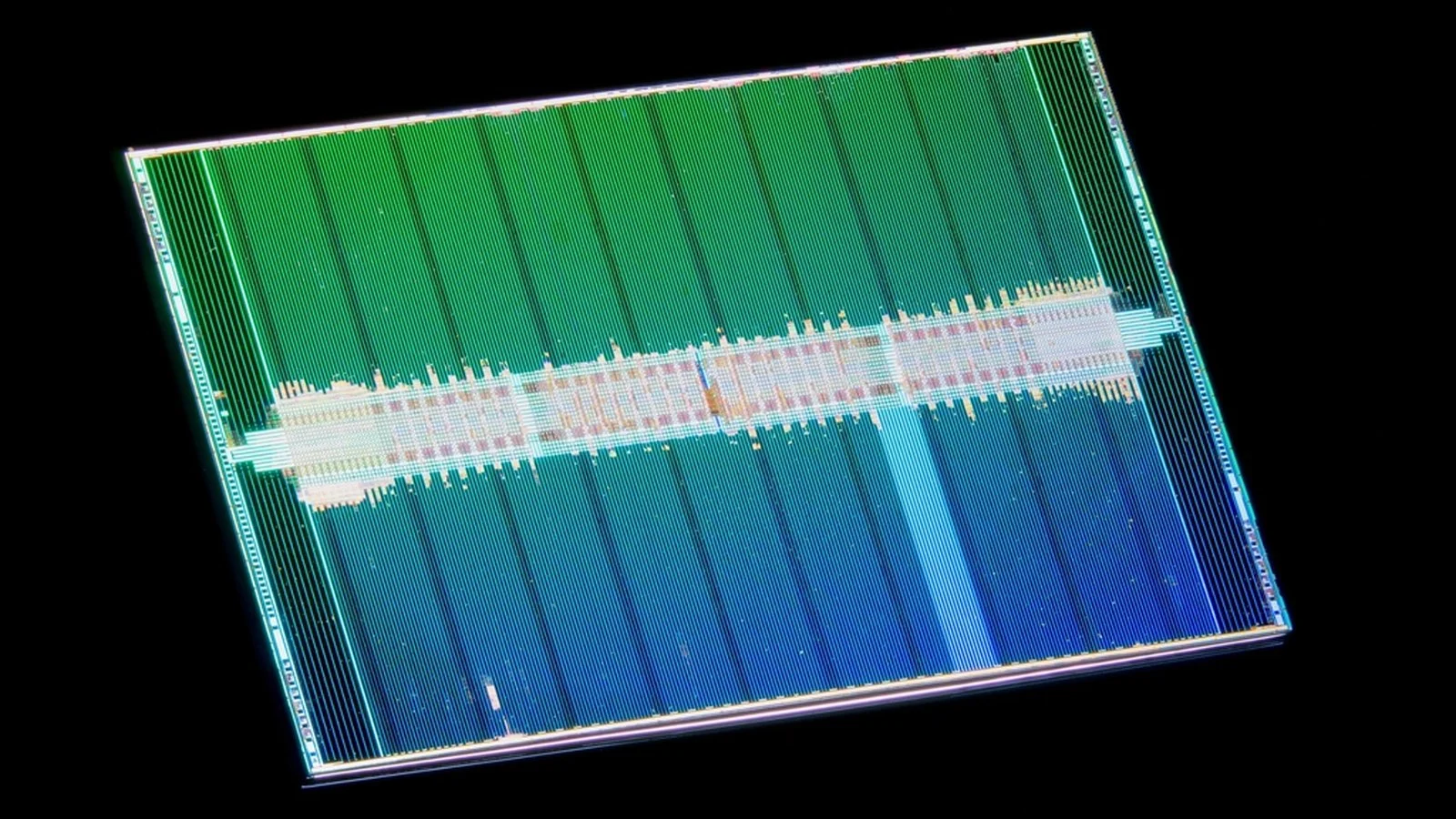 Macro photo of a rectangular silicon chip die with green and blue circuit block patterns