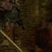 Person in medieval-style leather and chainmail armor holding a longsword near a stone ruin