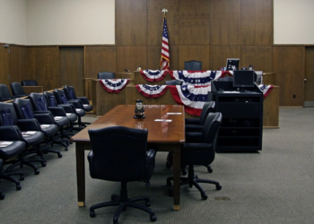 Empty wood-paneled courtroom with patriotic bunting, American flag, and jury chairs