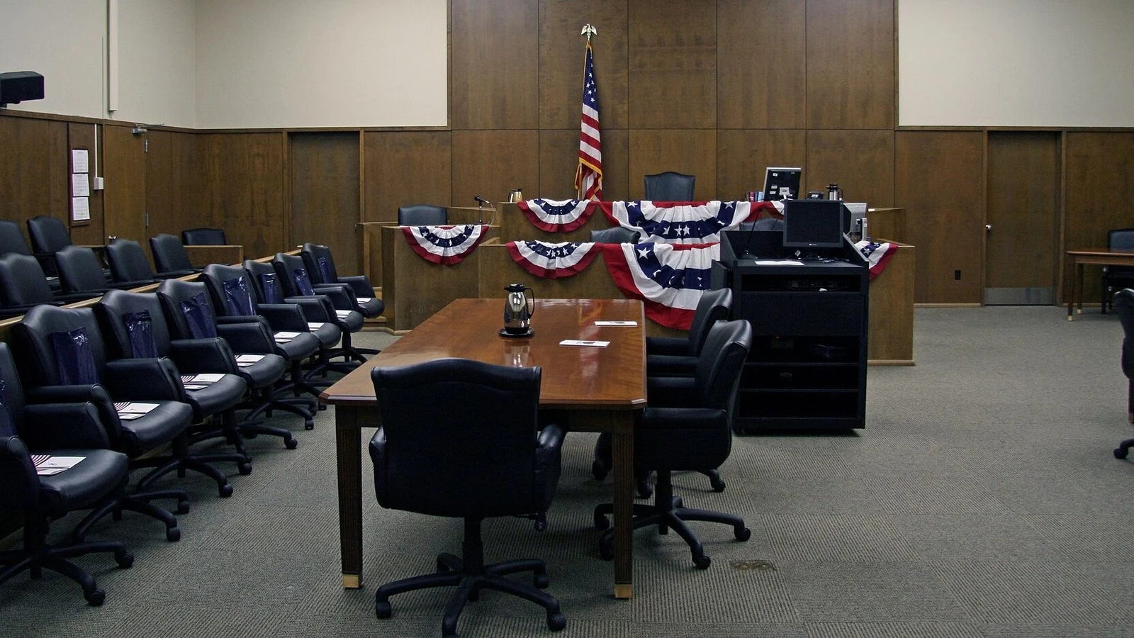 Empty wood-paneled courtroom with patriotic bunting, American flag, and jury chairs