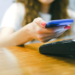 Woman taps a phone in a blue case against a wireless card payment terminal on a wooden counter