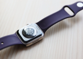 Apple Watch Series 7 with purple silicone band, face-down showing sensor cluster on a wood surface