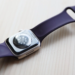 Apple Watch Series 7 with purple silicone band, face-down showing sensor cluster on a wood surface