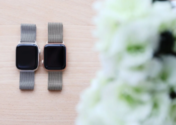 Two Apple Watches with metal mesh bands and dark screens lie on a wooden surface