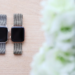 Two Apple Watches with metal mesh bands and dark screens lie on a wooden surface