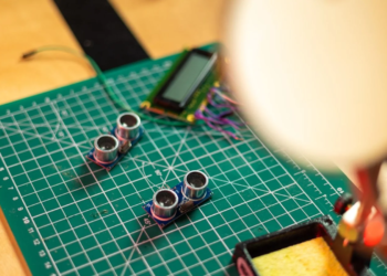 Ultrasonic sensor modules and a small LCD on a green cutting mat near a soldering iron