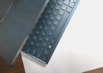 Close-up of a blue-grey ASUS laptop keyboard and lid edge on a wooden desk